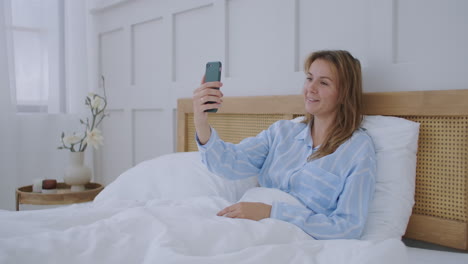 Businesswoman-having-a-video-call-in-hotel.-Happy-girl-lies-on-the-bed-talks-with-friends-via-video-call.
